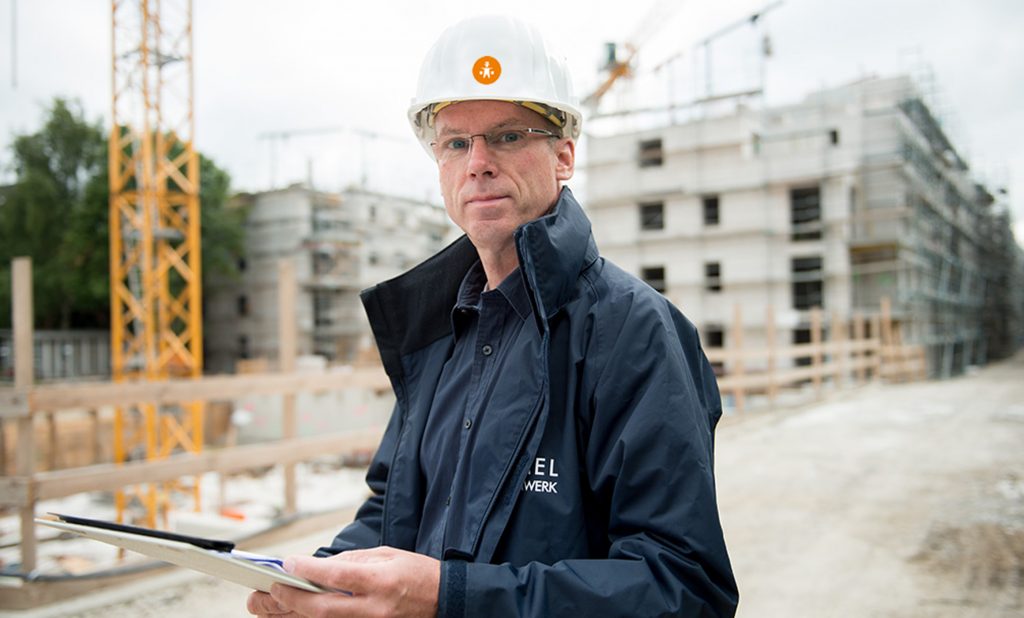 Hummel Küchenwerk Mitarbeiter mit Bauhelm steht vor einem Rohbau eines Mehrfamilienhauses.