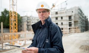 Hummel Küchenwerk Mitarbeiter mit Bauhelm steht vor einem Rohbau eines Mehrfamilienhauses.