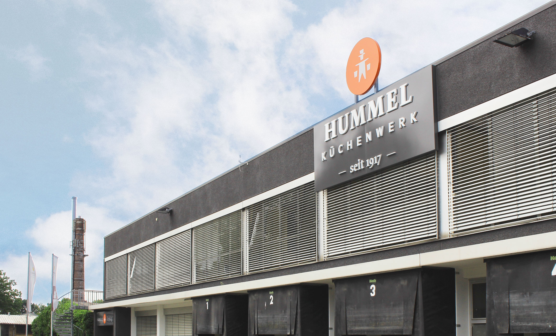 Fassade des Hummel Küchenwerks mit großem Logo. Flachdachbau aus den 70gern. Oben Büros unten Tore für Aus- und Anieferung.