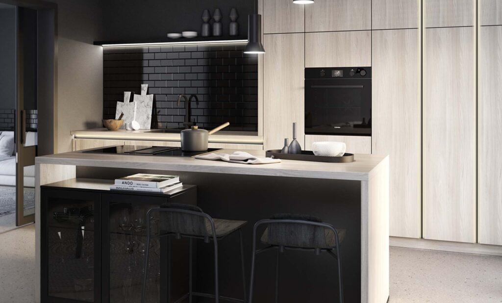 Kontrastreiche Küche mit hellem Holz und schwarzen Schrankelementen geplant. Im Vordergrund eine Kücheninsel an der schwarze Barstühle vor einer schwarzen Front stehen. Im Hintergrund eine Schrankzeile aus hellem Holz mit hochgebautem, schwarzen Backofen. Links davon ist eine Arbeitsfläche mit einer schwarzen, gläsernen Nischenrückwand geplant. Helle und dunkle Elemente sind im Verhältnis harmonisch geplant.