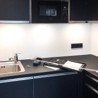 Neue schwarz-matte, L-förmige Hummel-Küche mit eingebauter Mikrowelle. Zollstock, Block und Laser auf der Arbeitsplatte.